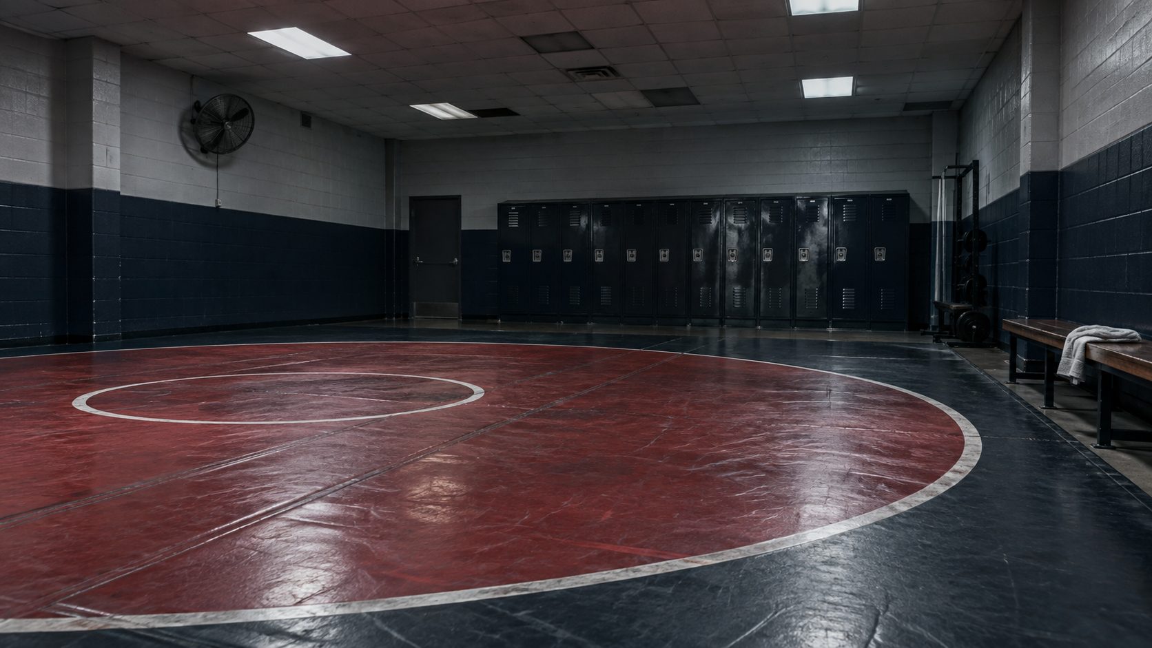 Illustrative: an empty high school wrestling room after hours — mat, lockers, and bench, the surfaces and storage a Shield3 program covers.